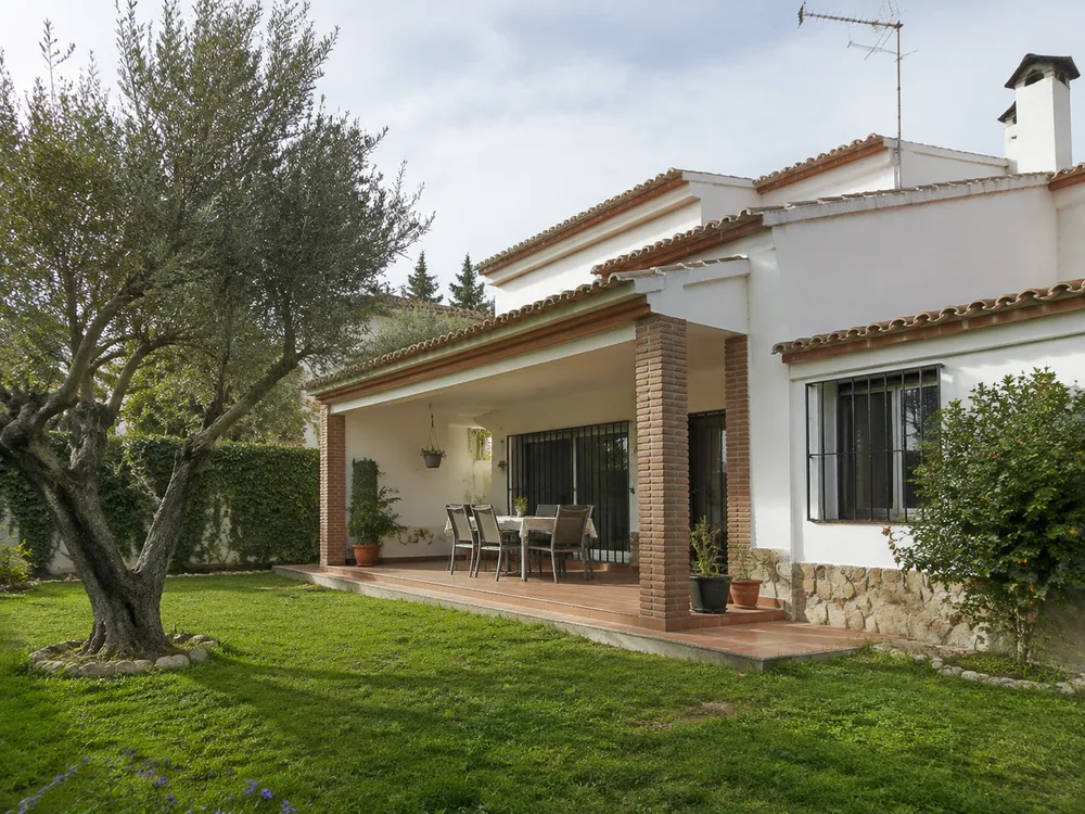 Casa de fachada blanca con un pequeño jardín y un olivo